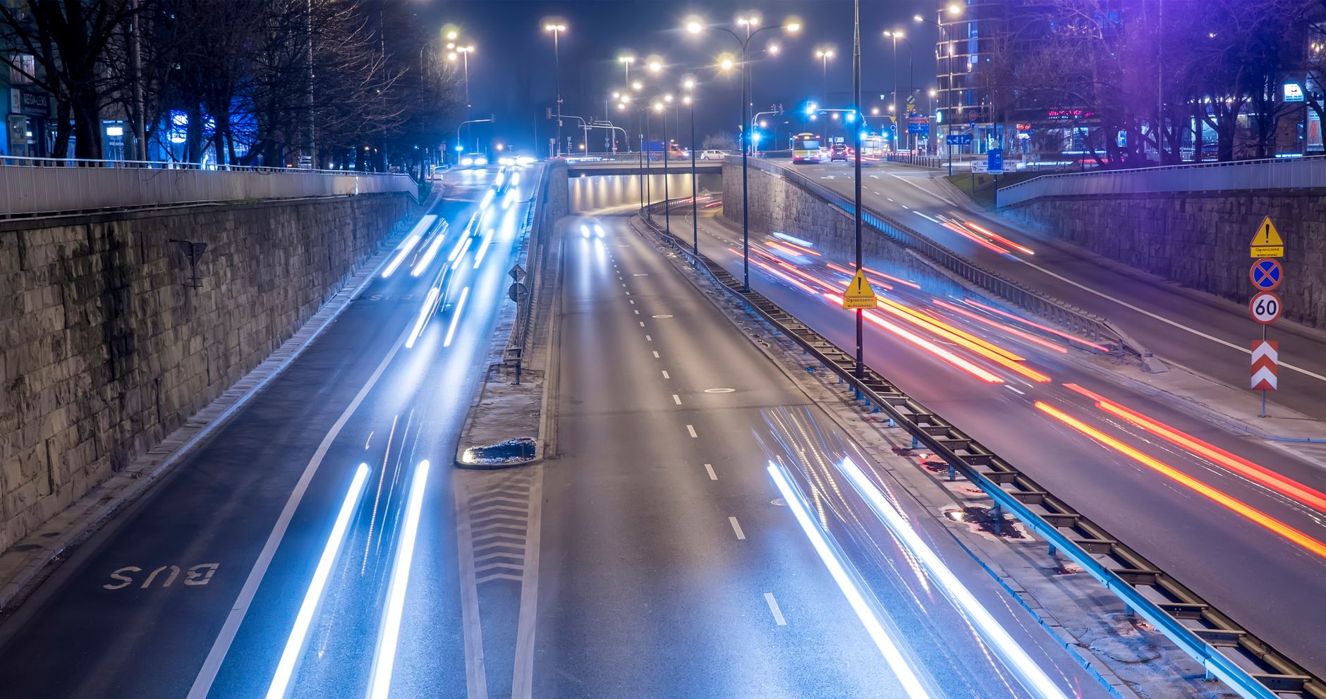 Long exposure photo capturing light trails of traffic on a busy Warsaw highway at night.