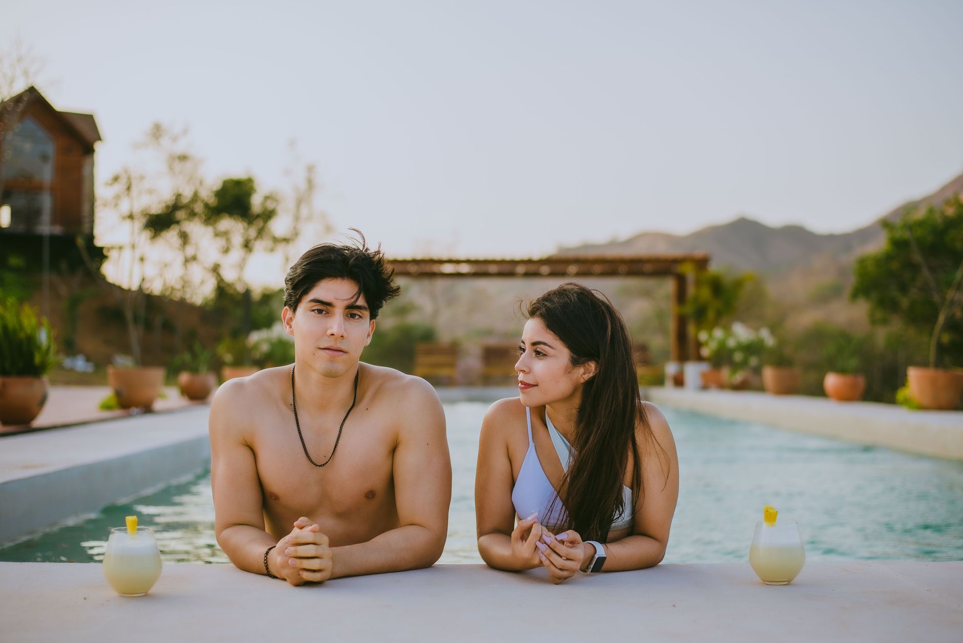 A couple enjoying a relaxing day by the pool in a summer resort setting, surrounded by nature.