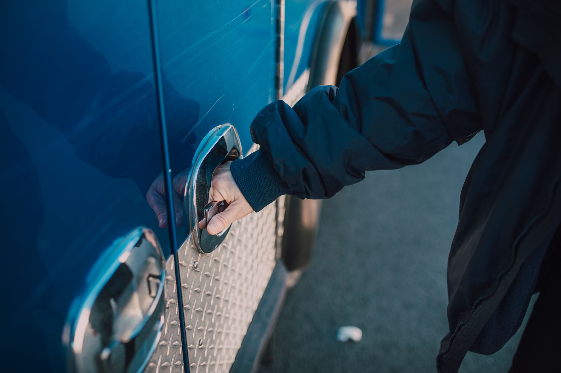 A person in a jacket opens a handle on a blue emergency vehicle, likely an ambulance.