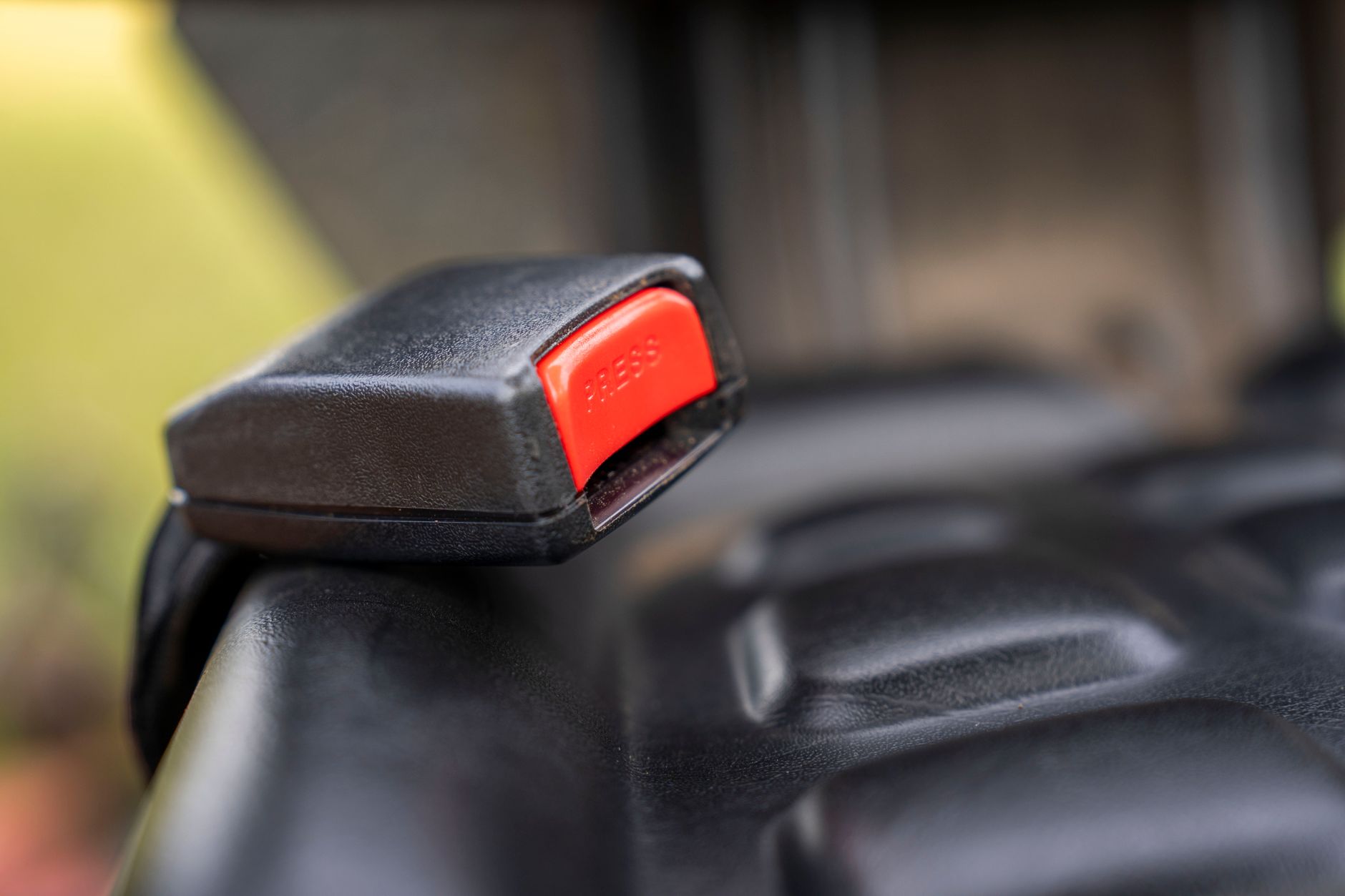 A detailed close-up image of a car seat belt buckle showing the red press button.