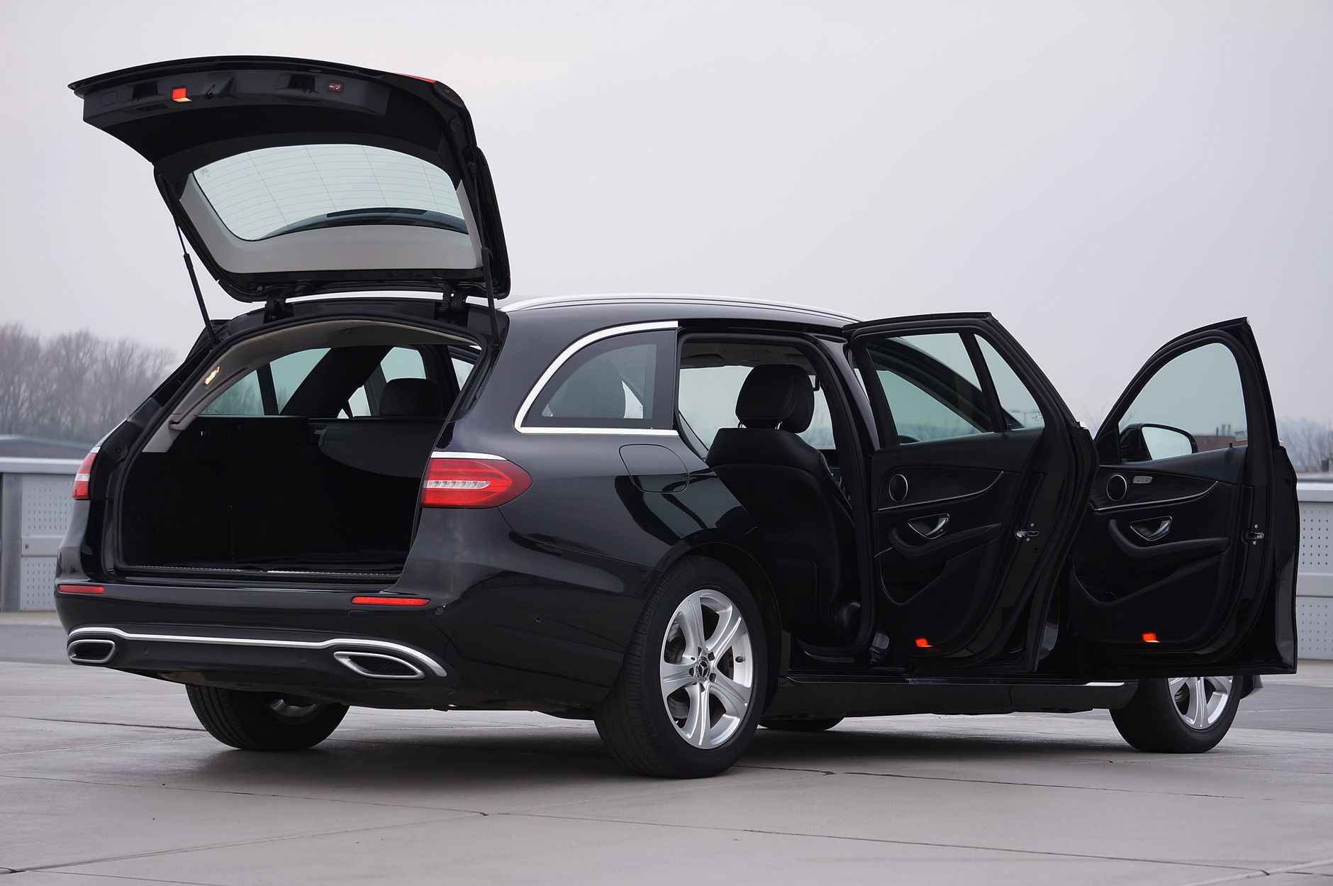 A sleek black car with doors and trunk open, parked outdoors in the UK, showcasing spacious interior.