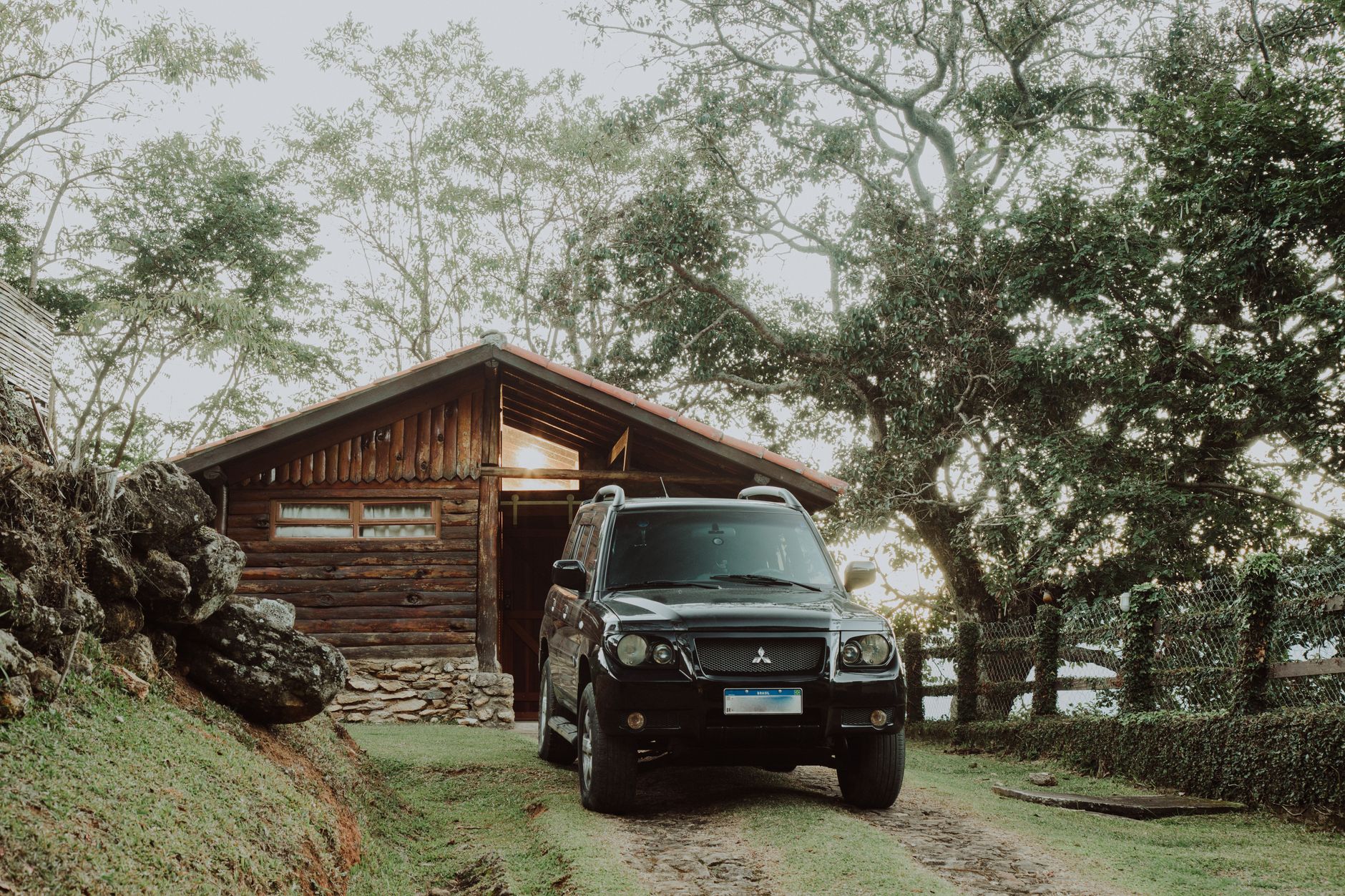 A black Mitsubishi SUV parked outside a wooden cabin surrounded by lush greenery.