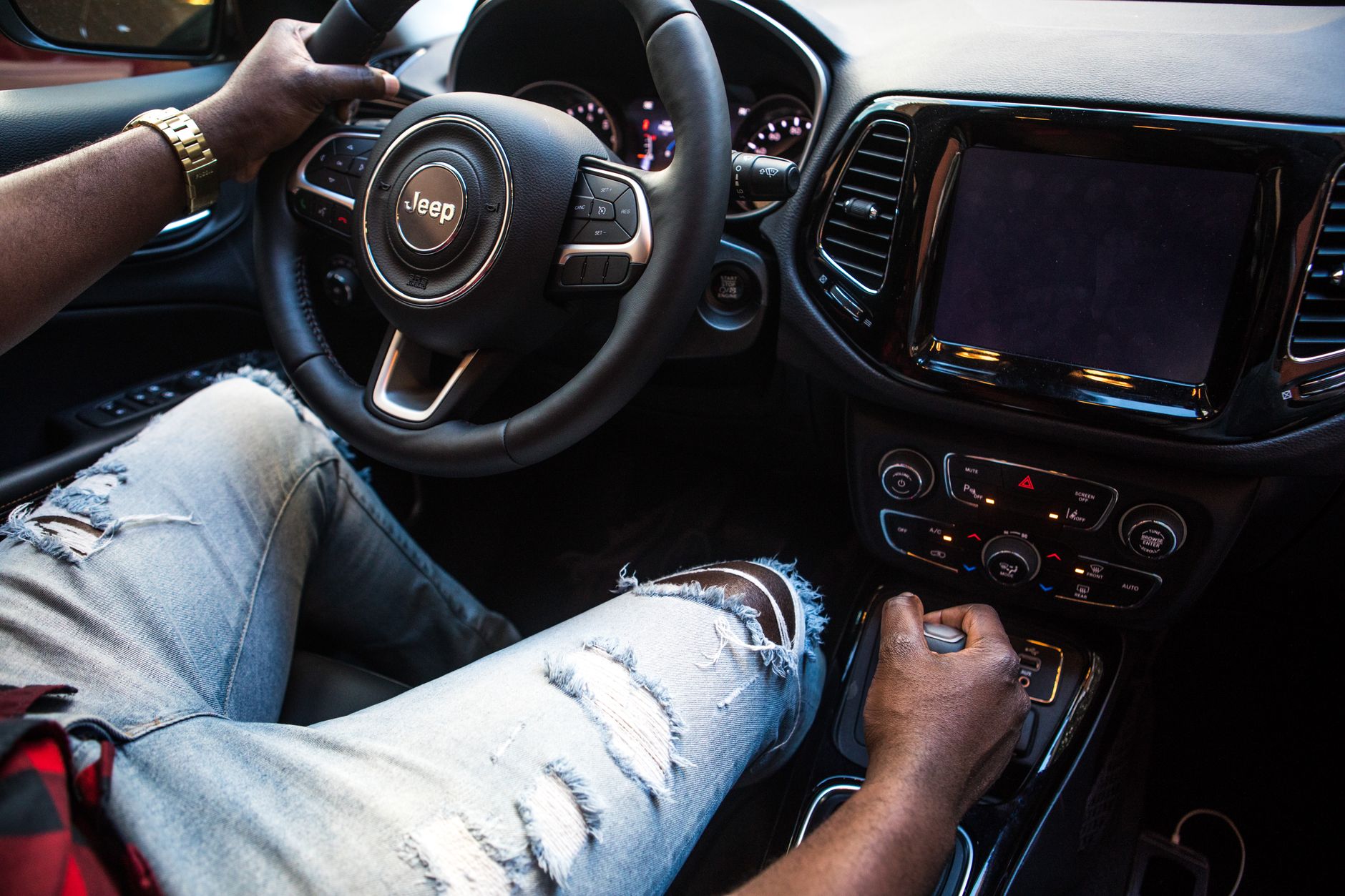 Interior view of a man driving a Jeep SUV with focus on the steering wheel and gear shift.
