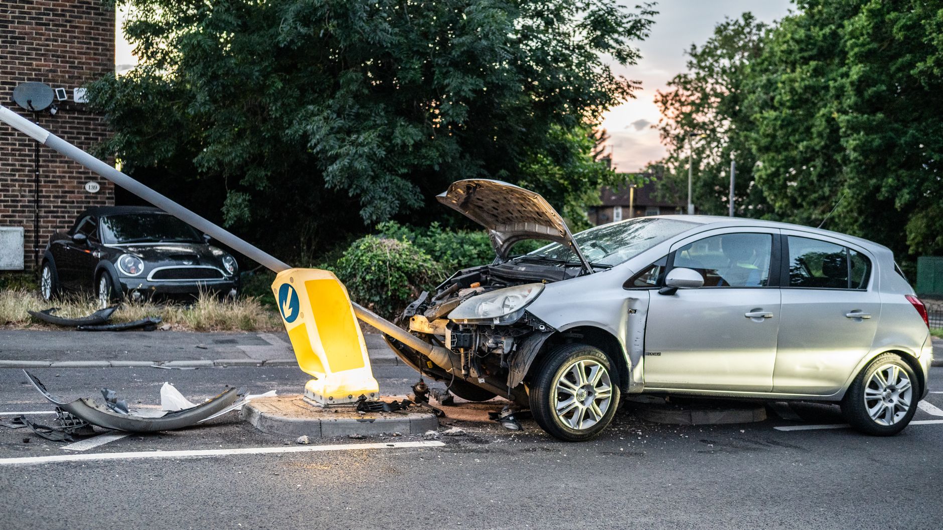 A damaged car that crashed into a lamp post on a London street during twilight.