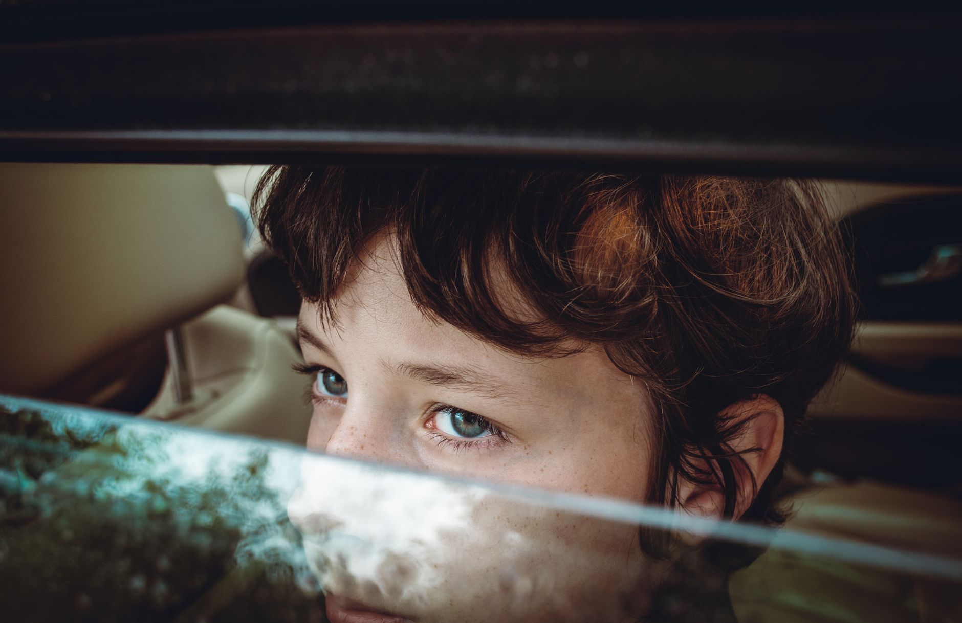 Close-up of a child with blue eyes looking out of a car window, reflecting a thoughtful mood.
