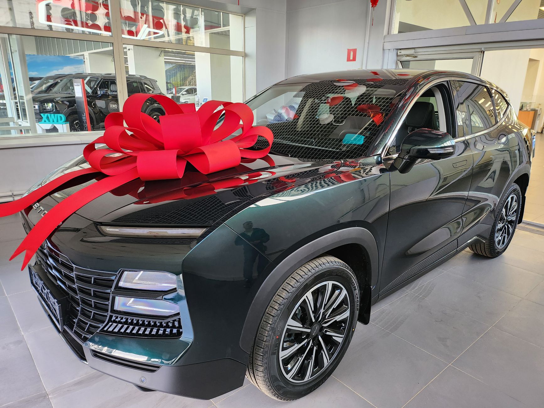 Shiny new SUV featuring a large red bow displayed in a modern car showroom.
