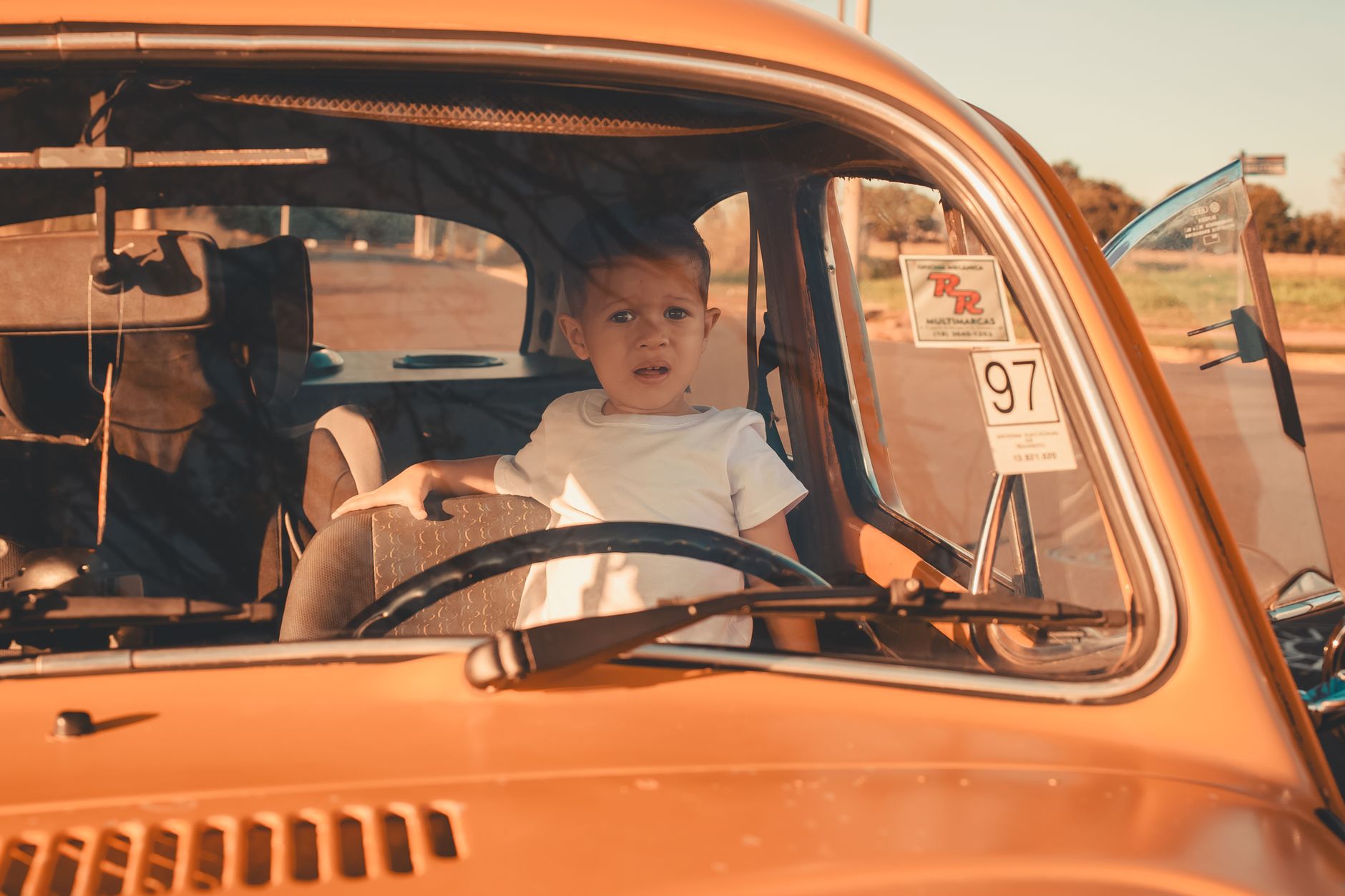 A child in a vintage car with a curious expression under warm sunlight.