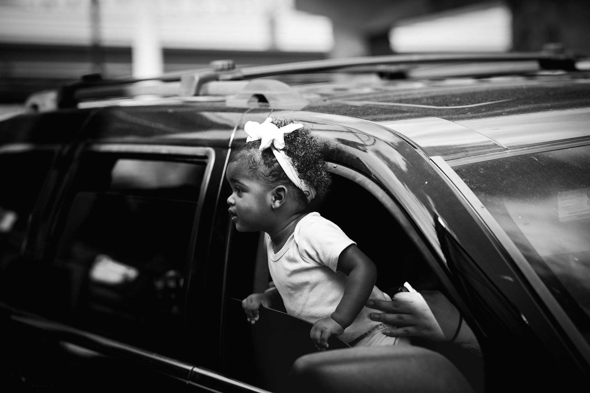 Black and white photo of a young child peering out of a car window with curiosity.
