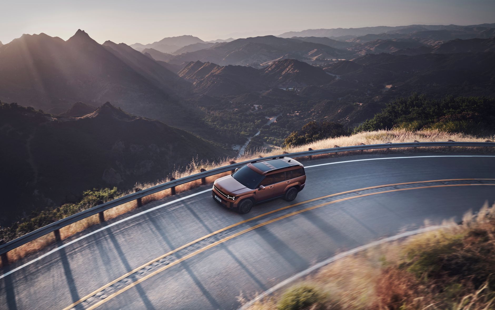 An SUV navigates a scenic mountainous road during sunset, offering breathtaking views and a sense of adventure.
