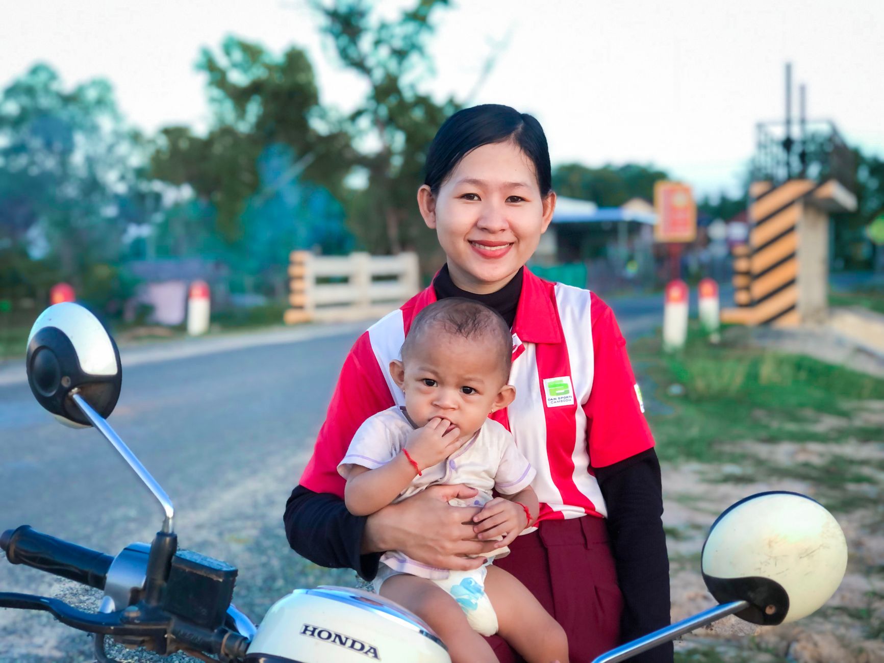 Smiling mother holding her baby on a motorcycle outdoors, capturing a joyful moment.