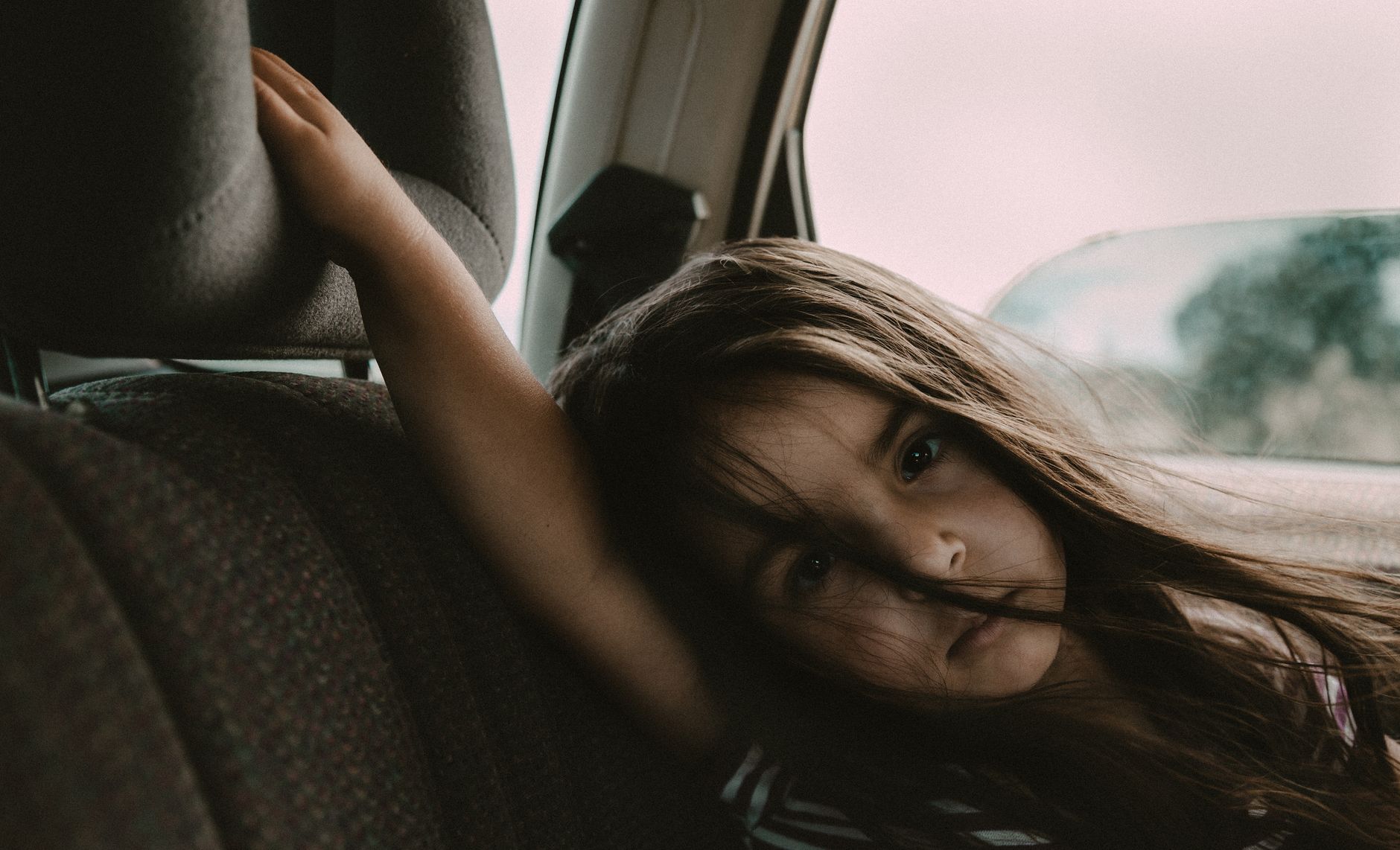 A young girl sits quietly in a car, gazing pensively out the window.