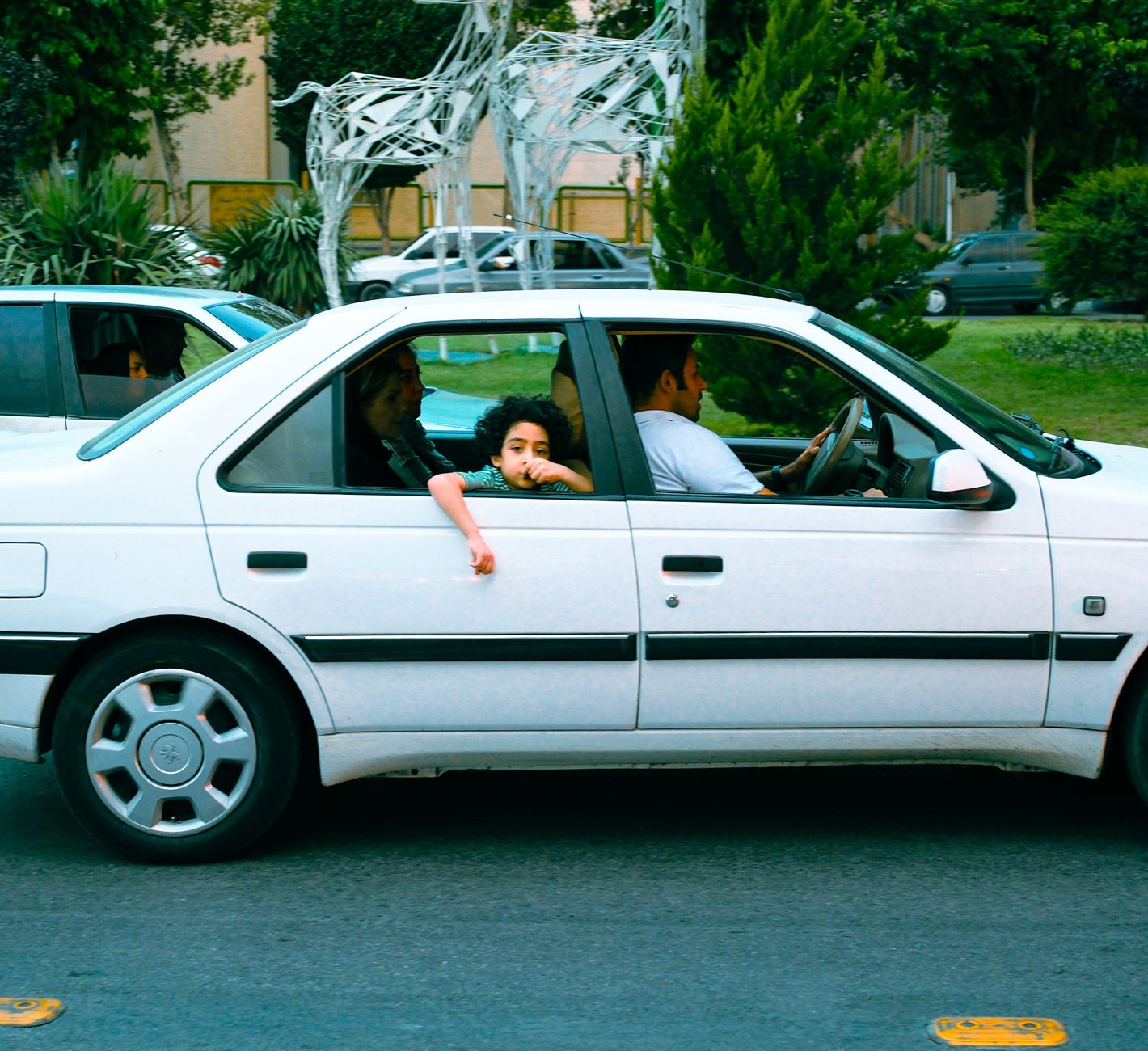 A family on a car ride, including a child looking out the window, in an urban setting.