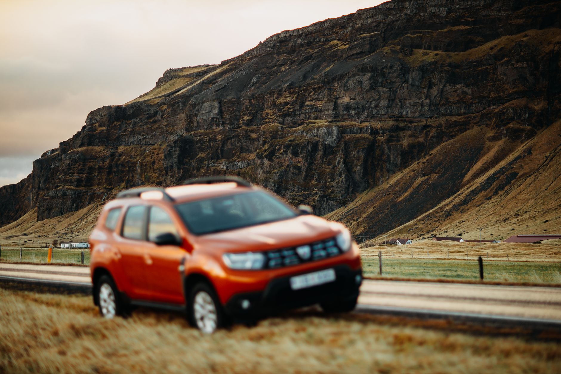 An orange SUV parked on a rural road beside a rugged hillside, captured in a scenic outdoor setting.