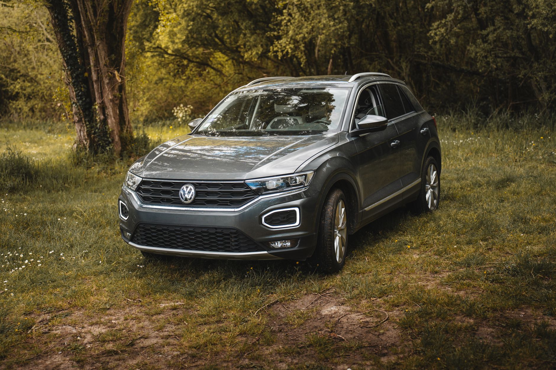 A modern Volkswagen T-Roc SUV parked in a picturesque forest meadow on a sunny day.