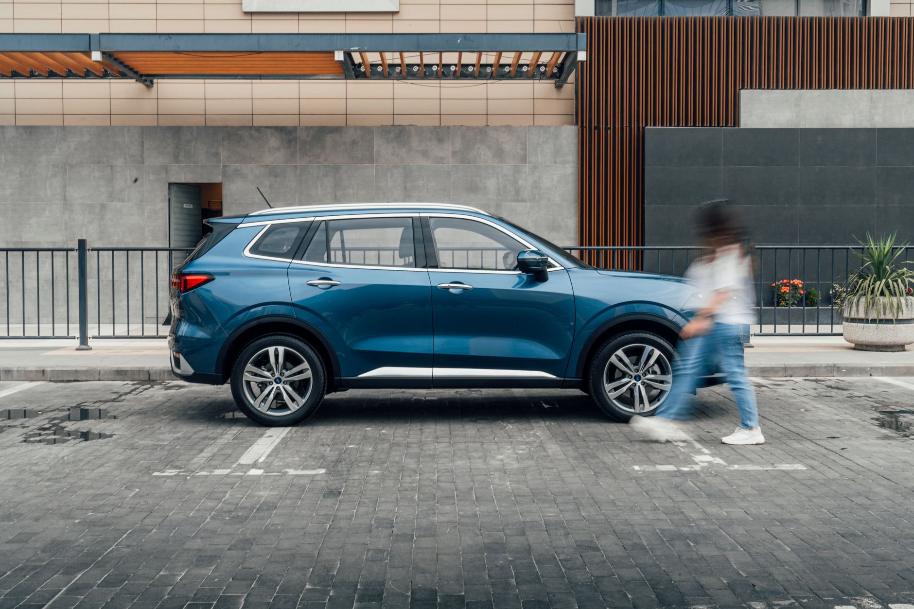 A blue SUV parked on a city street with a blurred pedestrian in the foreground.