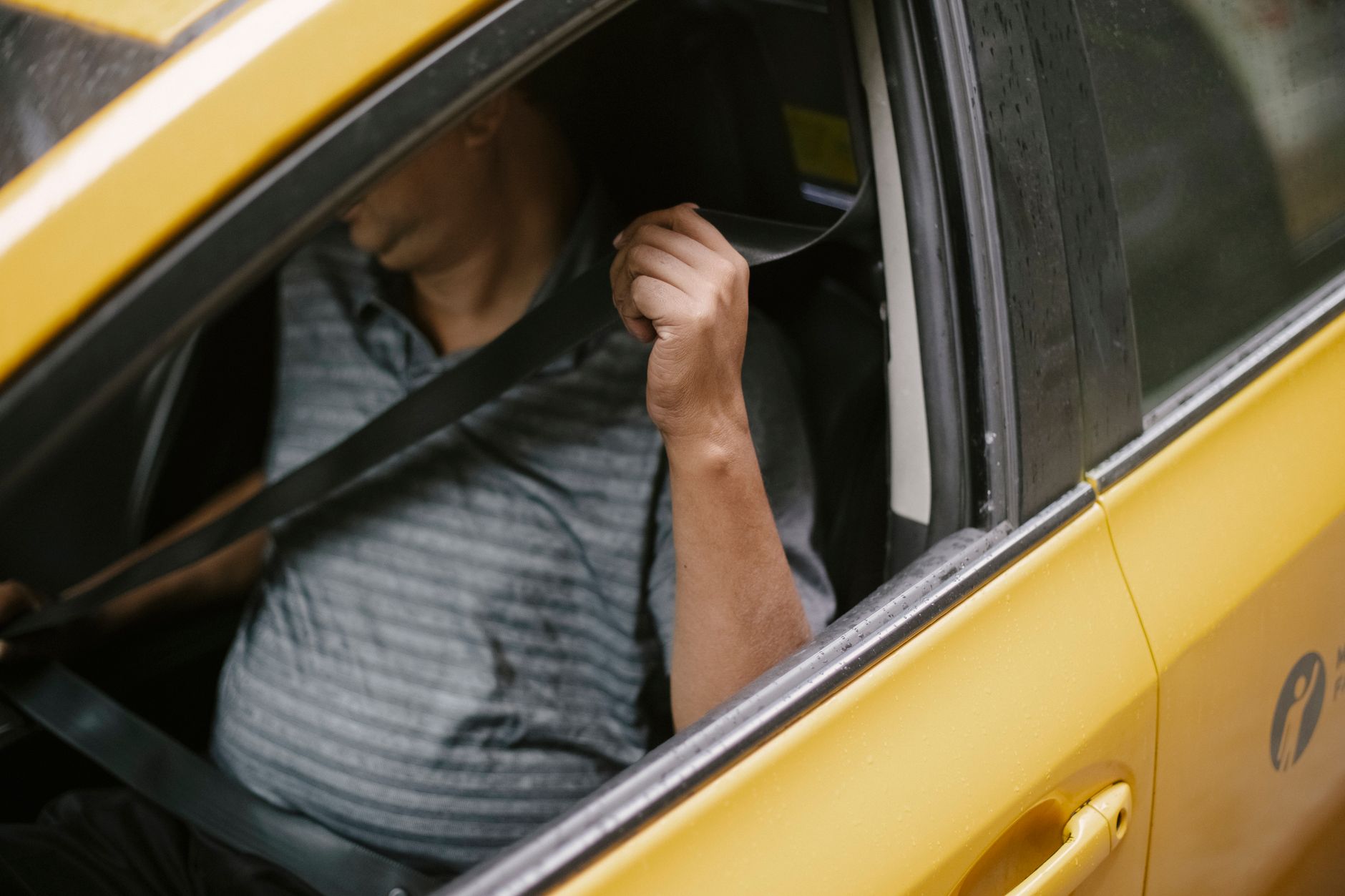 High angle of anonymous middle aged man in casual clothes fastening seat belt before riding yellow taxi parked on street