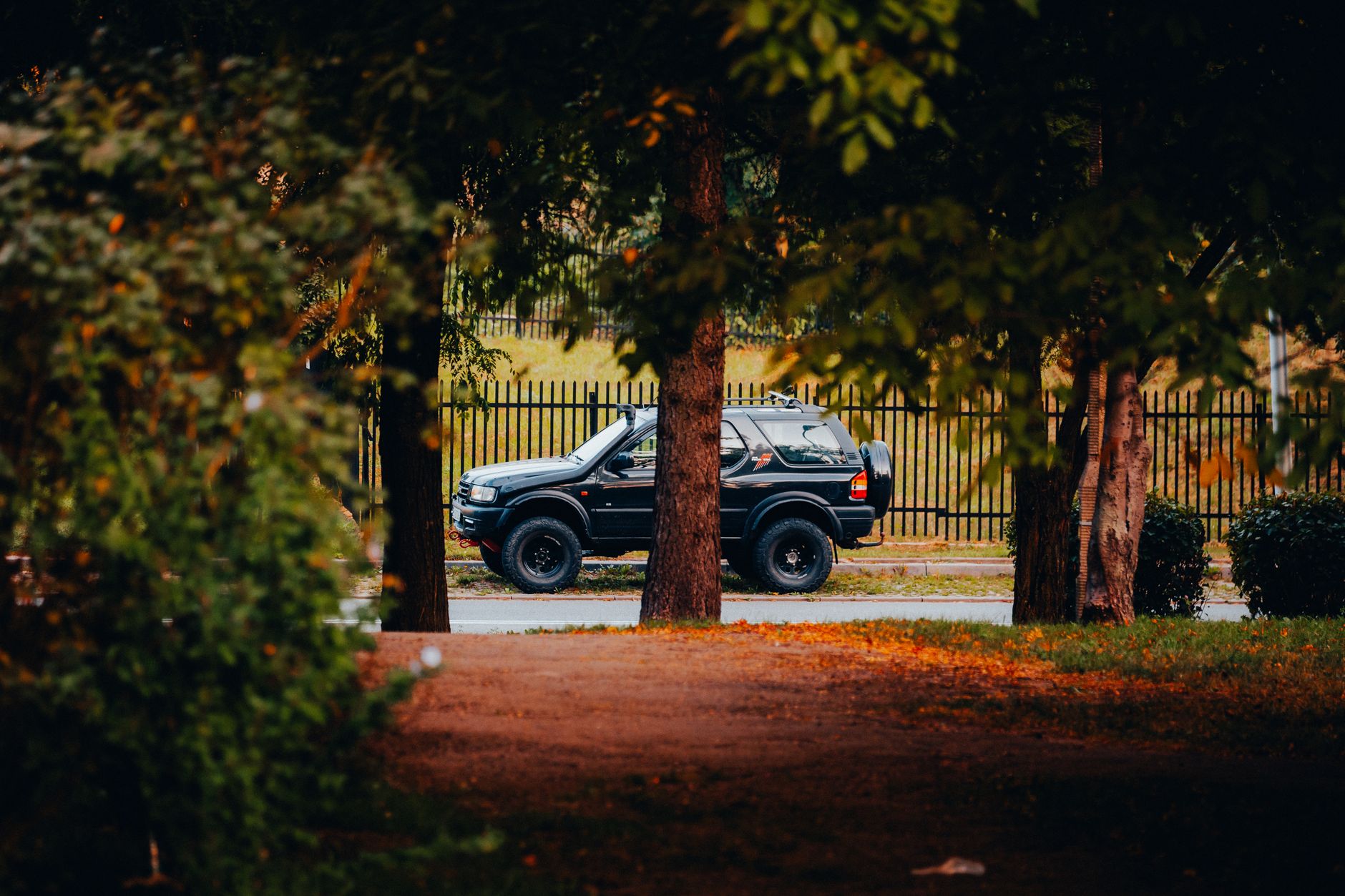 A black 4x4 SUV parked on a road surrounded by lush green trees and countryside.