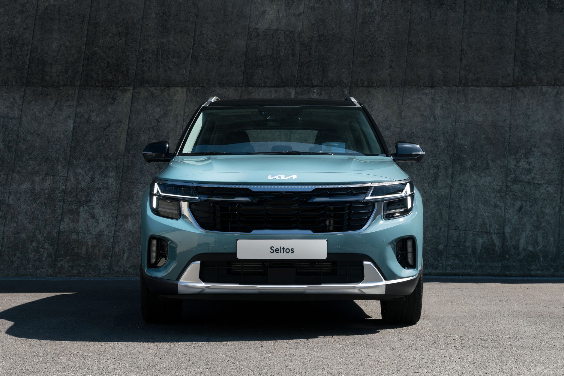 A modern blue Kia Seltos SUV parked against a concrete wall in daylight.