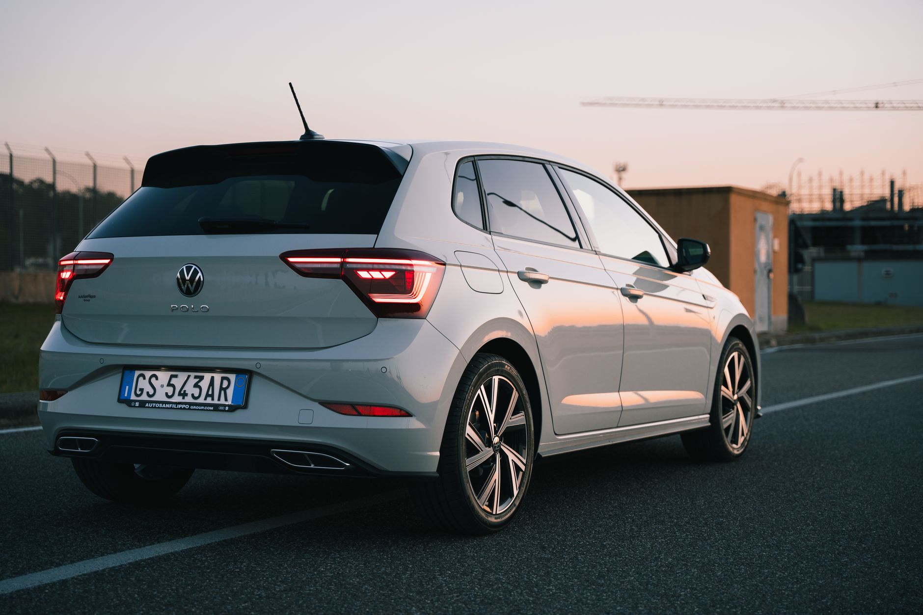 A sleek Volkswagen Polo parked on a road during sunset, showcasing its stylish design and urban environment.