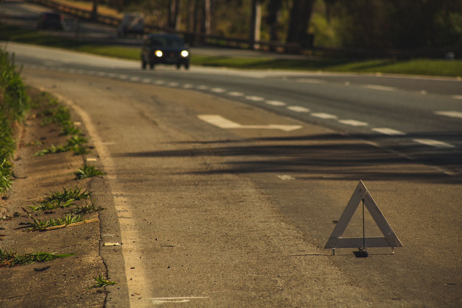 Automobile with headlights on driving on asphalt road with triangular sign in twilight