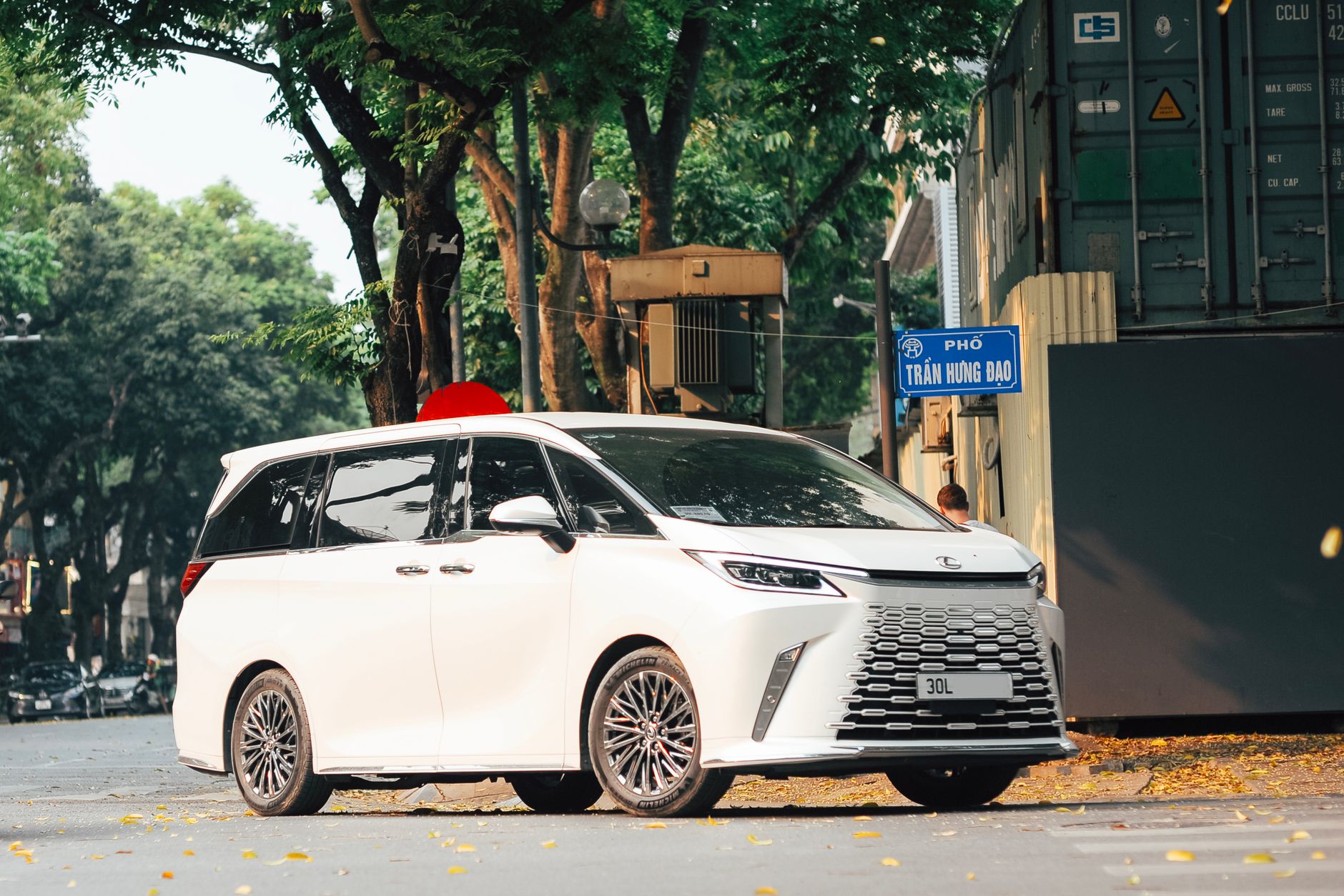 A sleek white minivan parked on a city street corner with tree-lined surroundings.