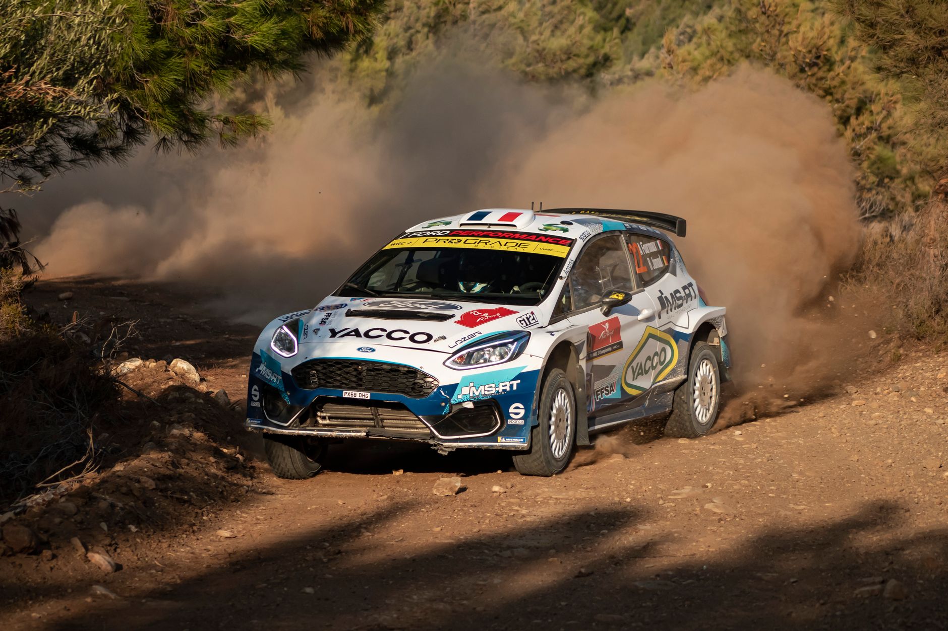 Rally car speeds through a dusty countryside track, showcasing agility and power.