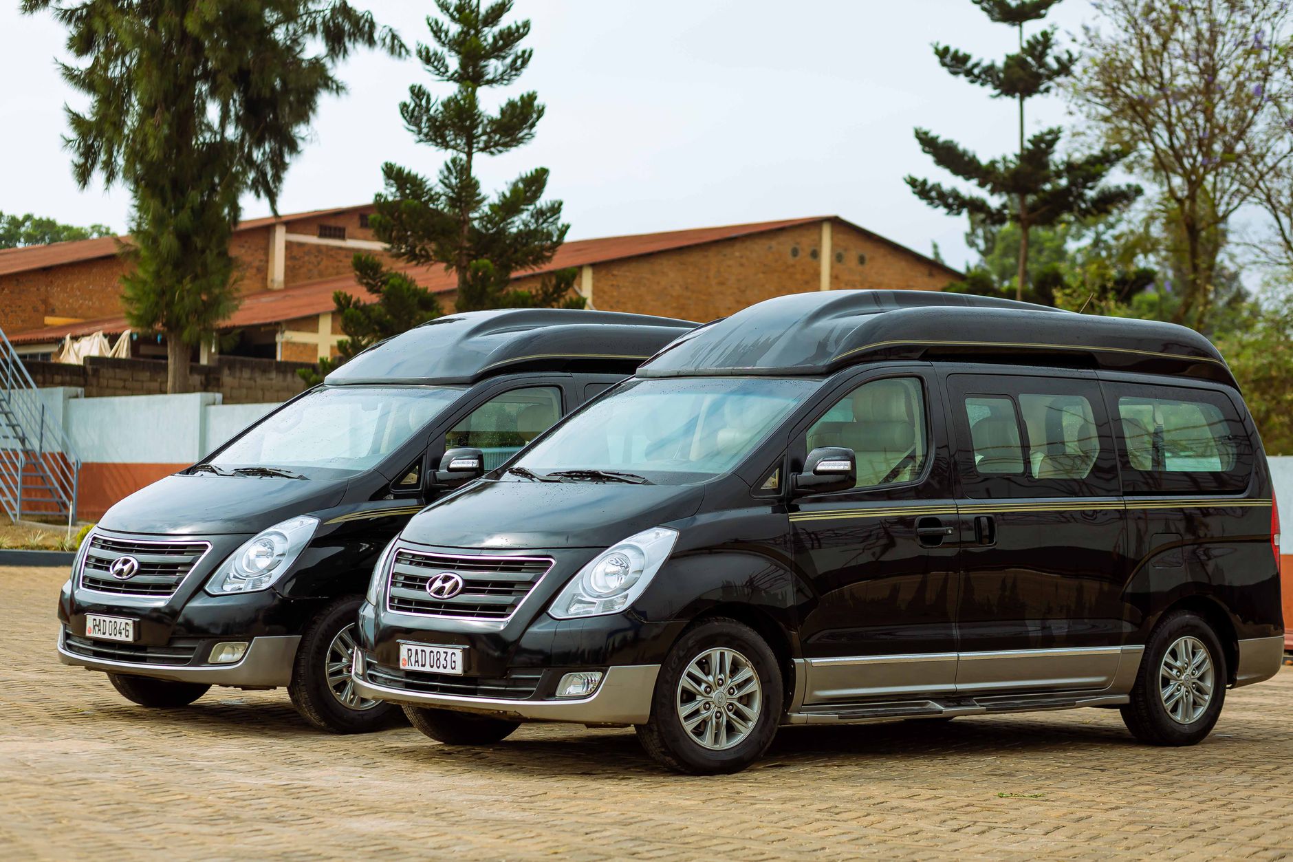 Two black Hyundai vans parked outdoors in a sunny summer day with trees in the background.
