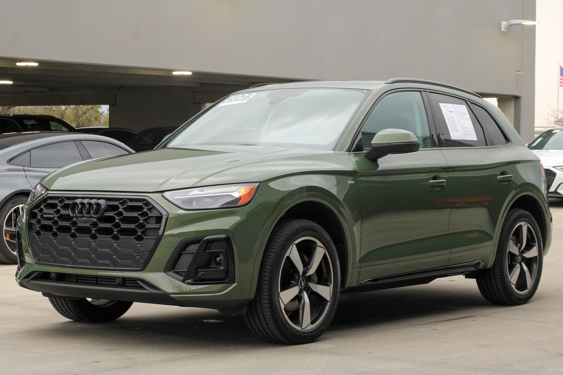 Modern khaki green 2024 Audi Q5 SUV parked in an urban parking lot, showcasing sleek automotive design.