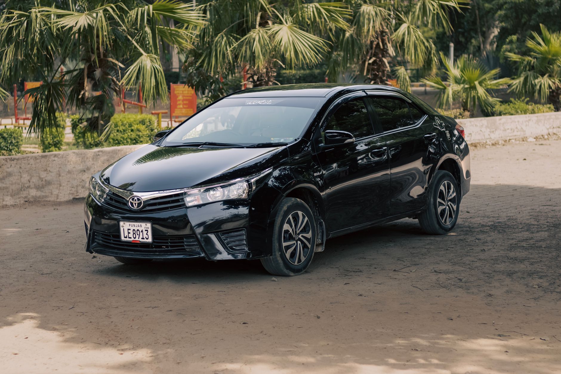 A stylish black Toyota Corolla parked outdoors amid lush tropical greenery, showcasing its elegant design.