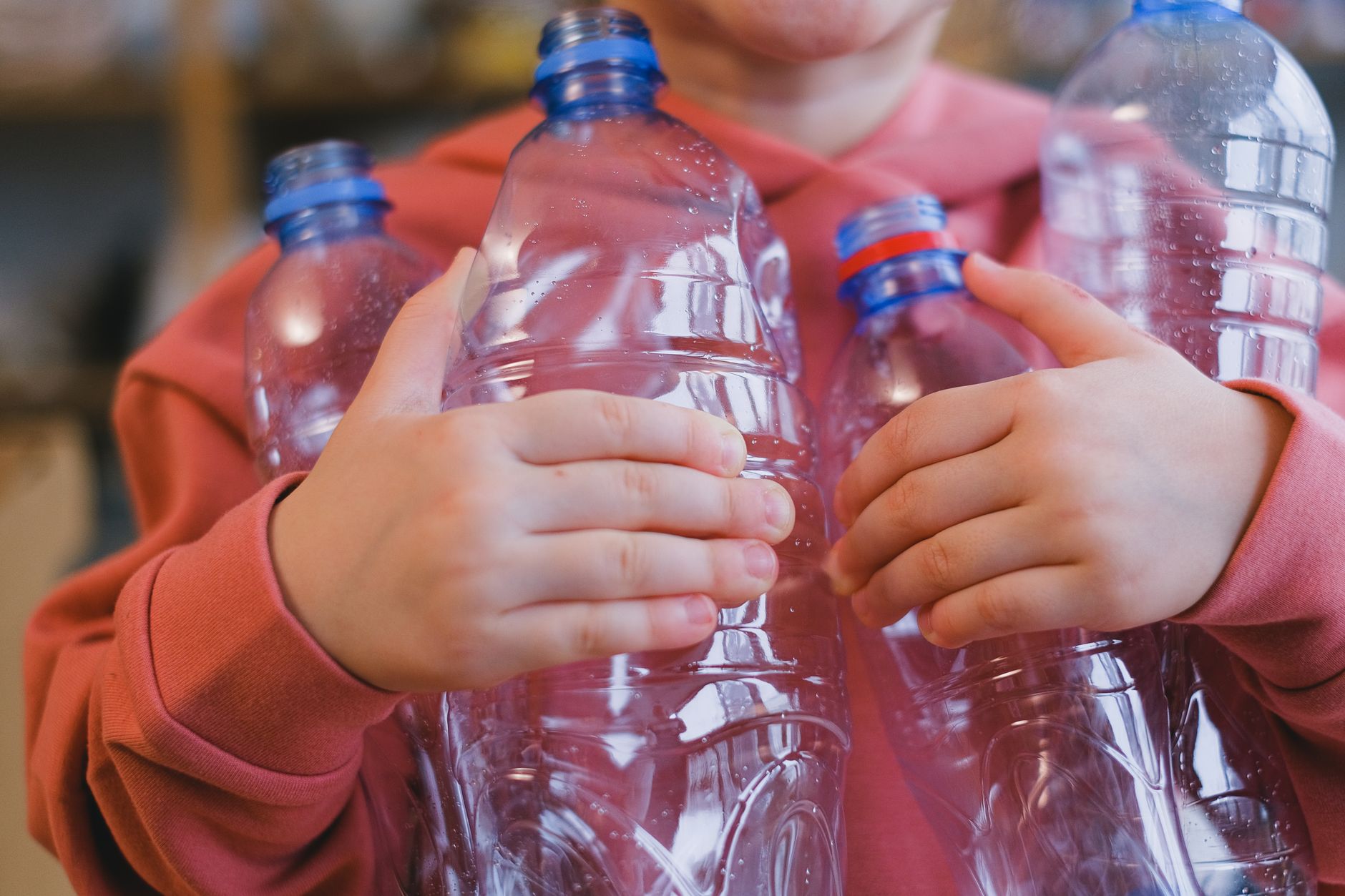 A child in a pink hoodie holding multiple recyclable plastic bottles, emphasizing zero waste and sustainability.