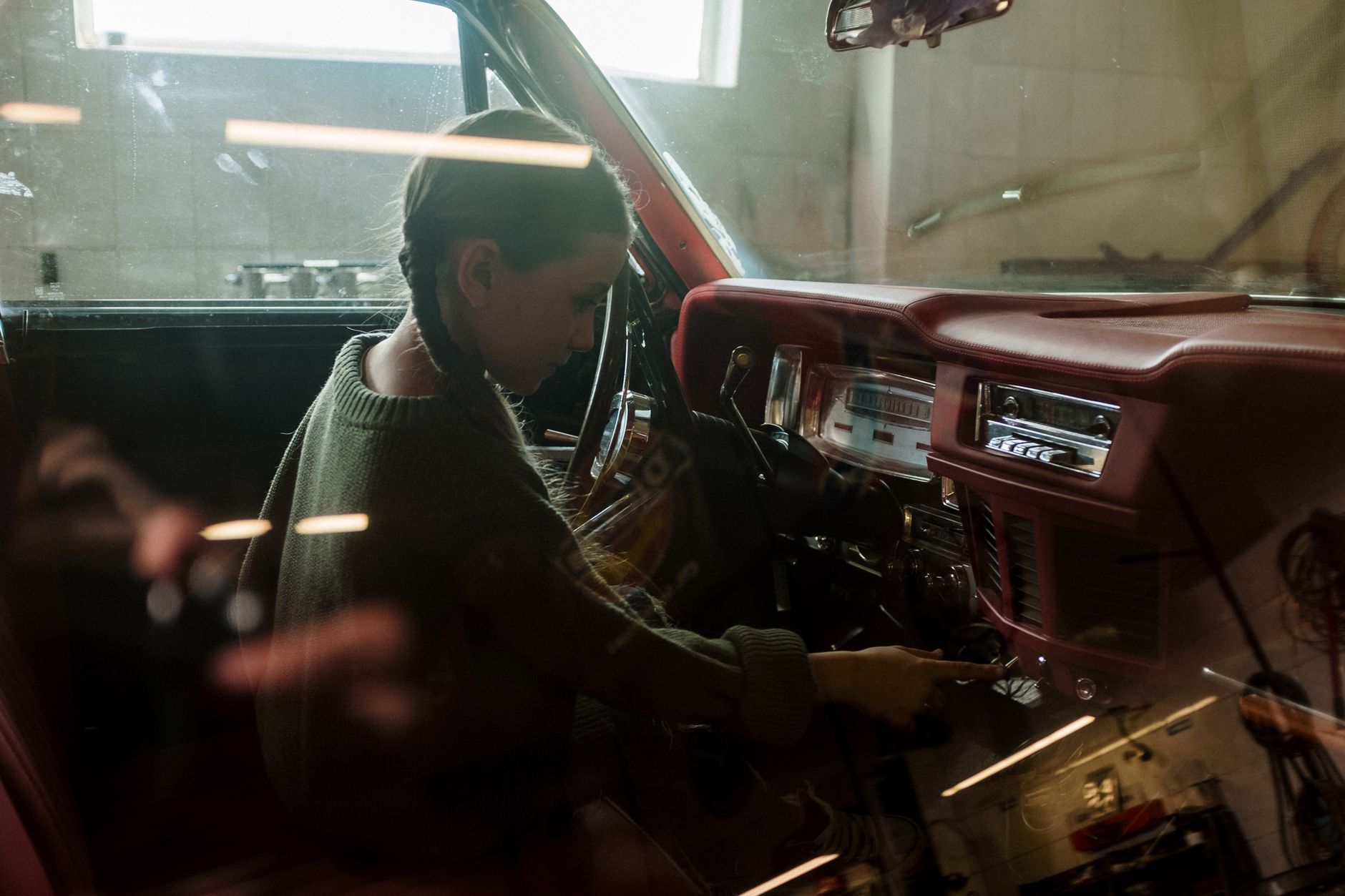 Young girl with pigtails interacts with a vintage car's dashboard indoors.