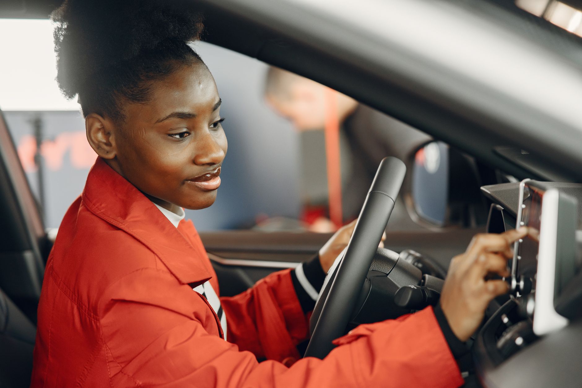 Young woman in red coat using touch screen in car interior.