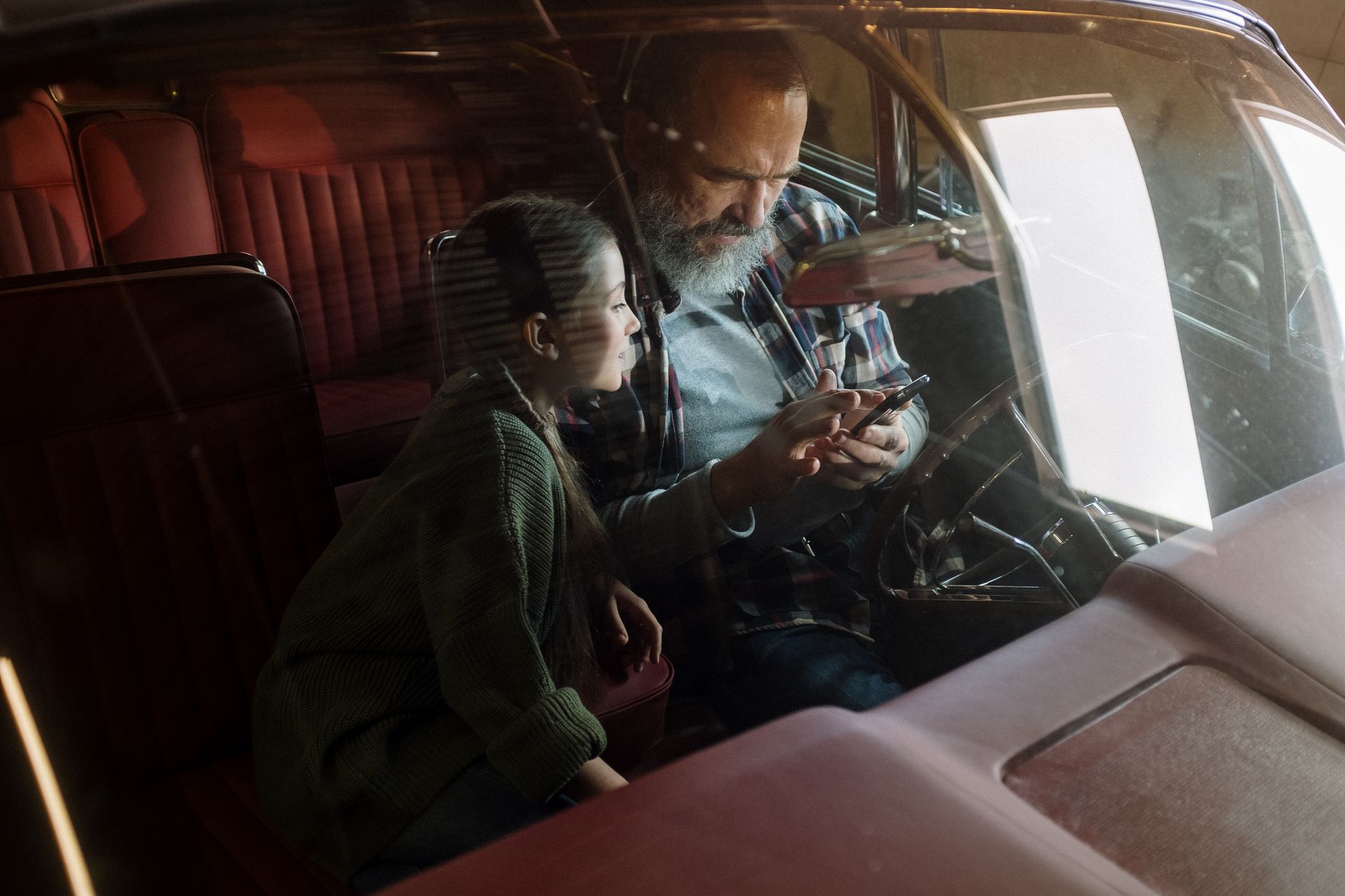 Father and daughter bonding in vintage car, viewing a smartphone together with cozy ambiance.