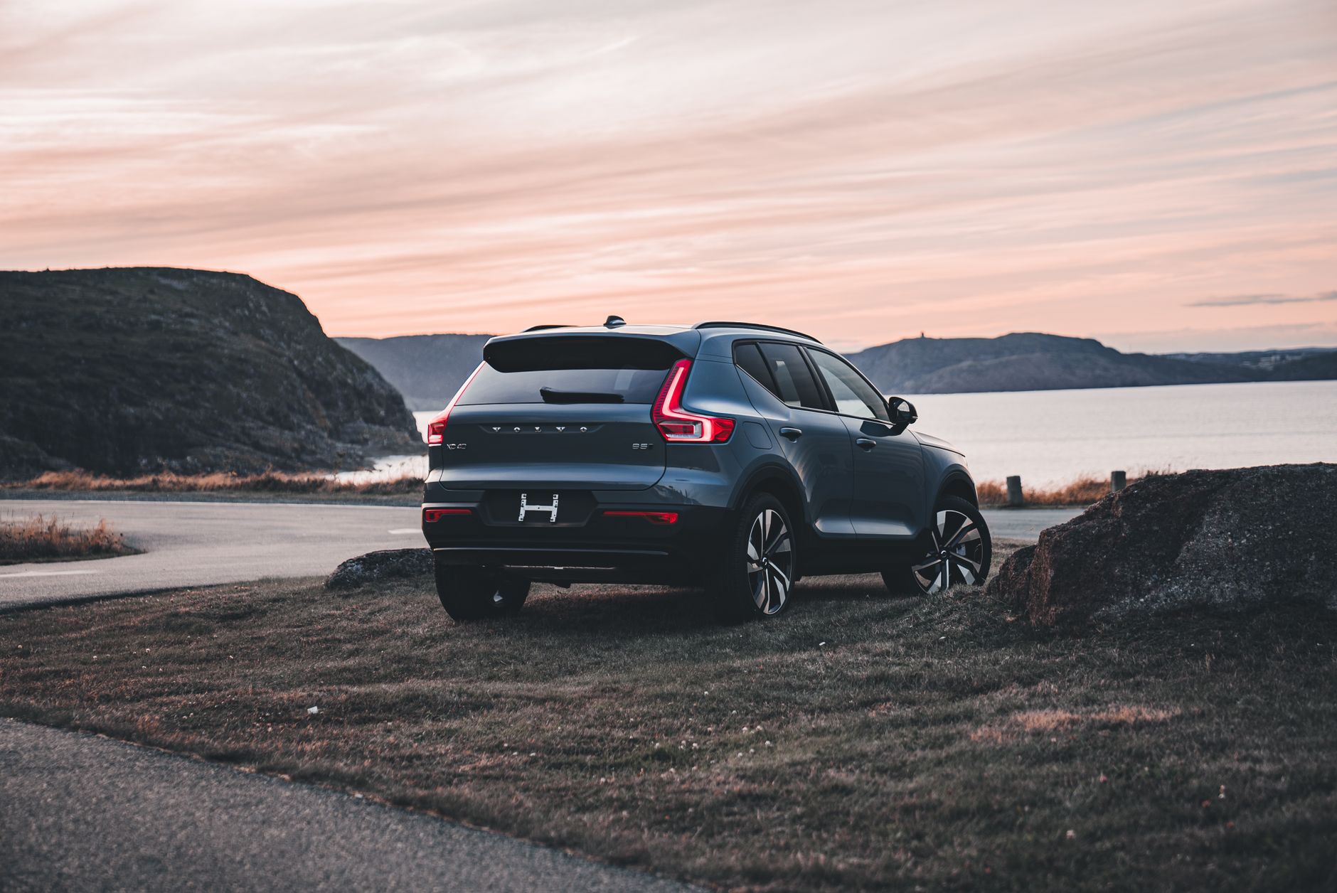 A Volvo XC40 SUV parked near a scenic bay during a serene sunset, highlighting its elegant design and outdoor backdrop.
