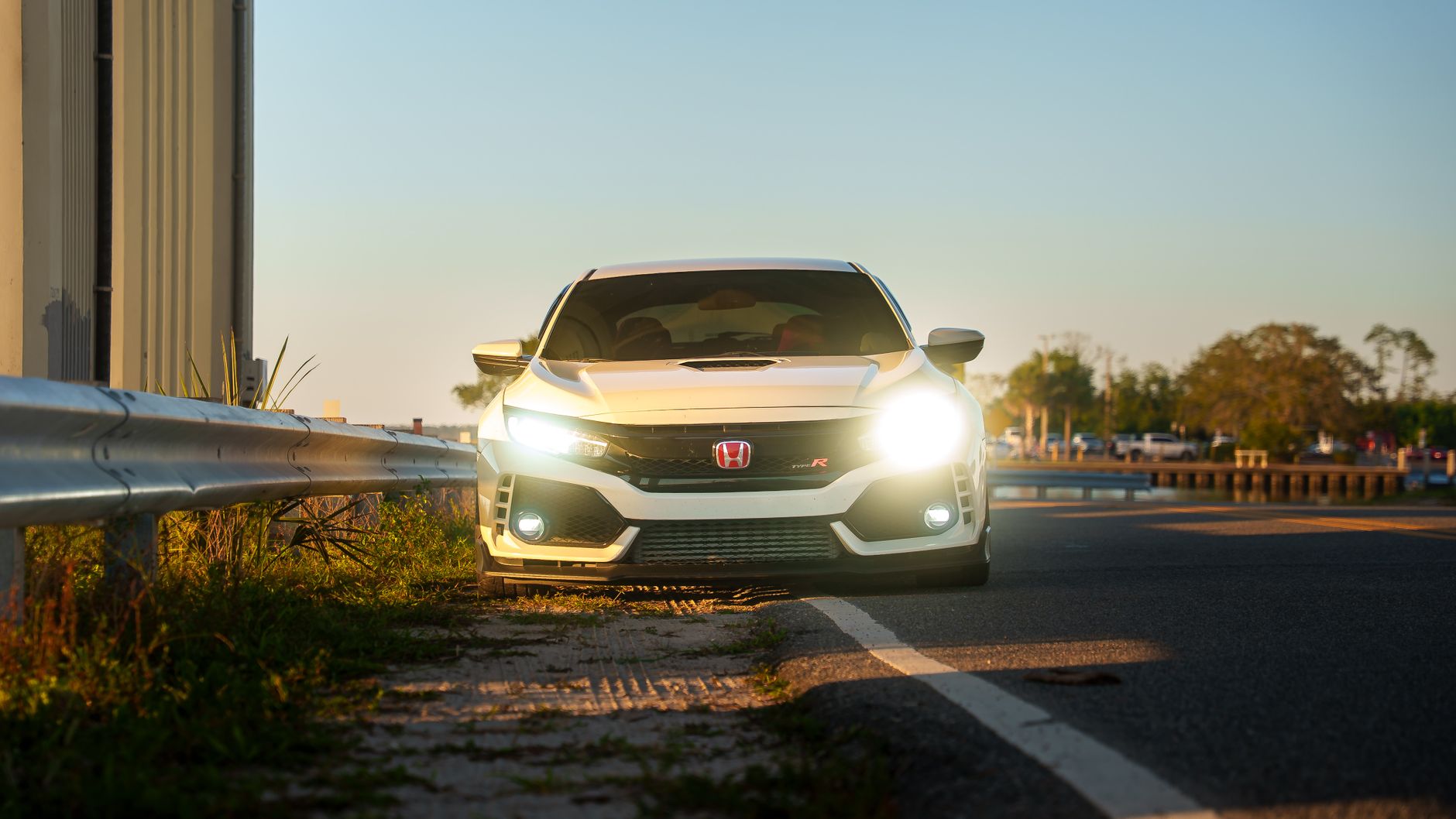 A sleek white car with headlights on, parked along a scenic highway at sunset.