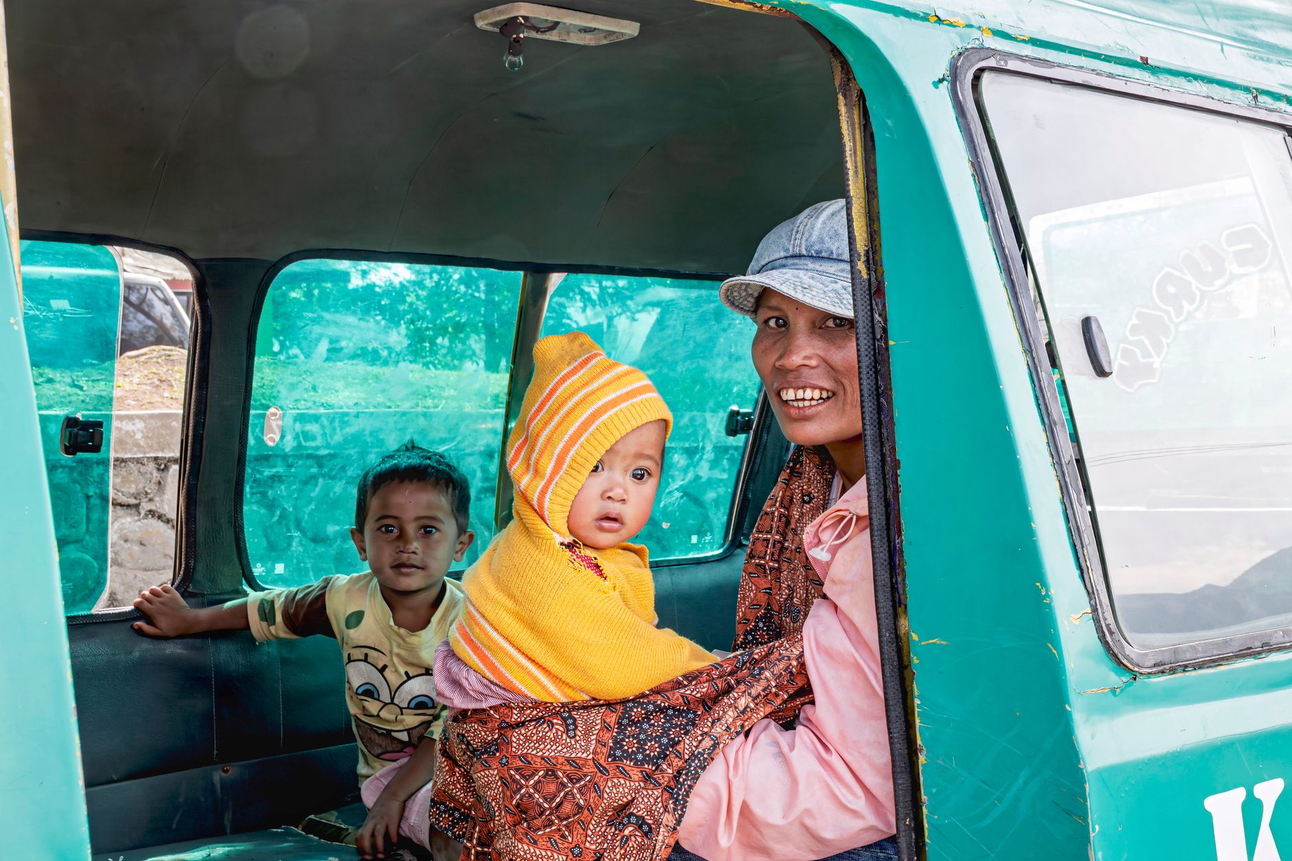 A family with children inside a green minivan in Indonesia. Smiling faces and vibrant colors.