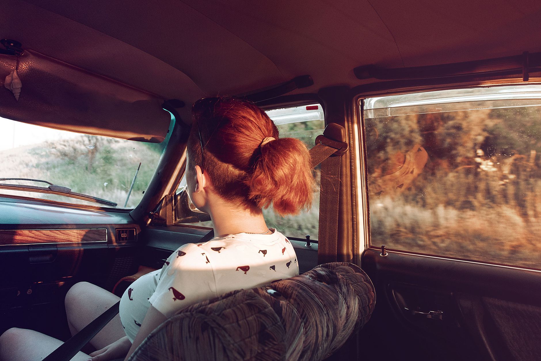 View from backseat on back view of anonymous female with red hair sitting on passenger seat buckled up while riding in vintage automobile on